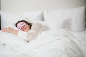 Egy hölgy, szemkötővel a fején alszik egy ágyban. Azért mert az alvás és a szex összefügg.